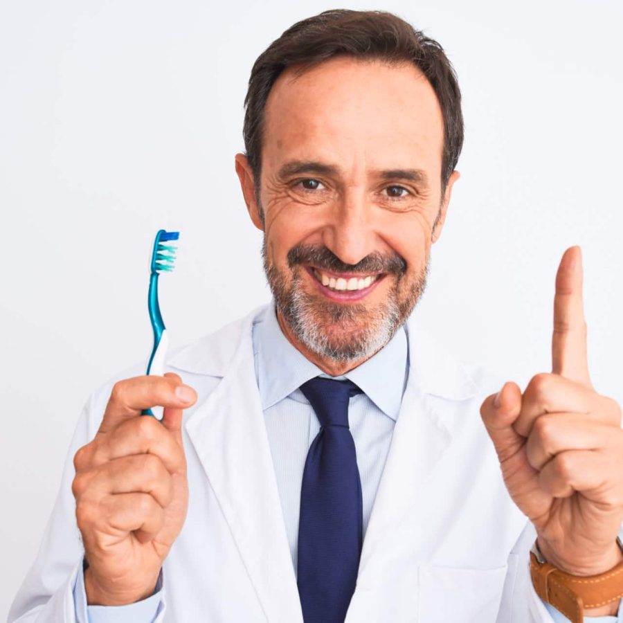 Middle age dentist man holding toothbrush standing over isolated white background surprised with an idea or question pointing finger with happy face, number one